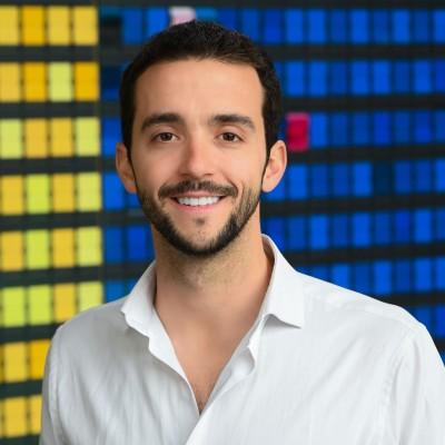 Portrait of a smiling man in a white shirt with a data center backdrop of colorful racks behind him.