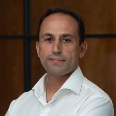 Portrait of a man in a white dress shirt looking at the camera against a brown background.