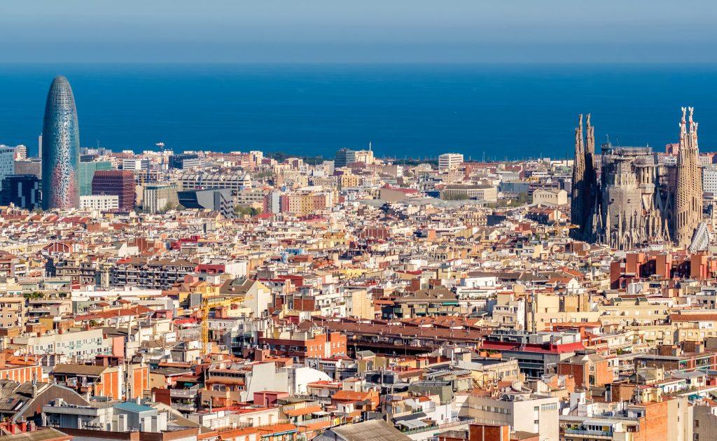 Cityscape of Barcelona with the Sagrada Família on the right and Torre Glòries on the left, sea in the distance under a clear blue sky