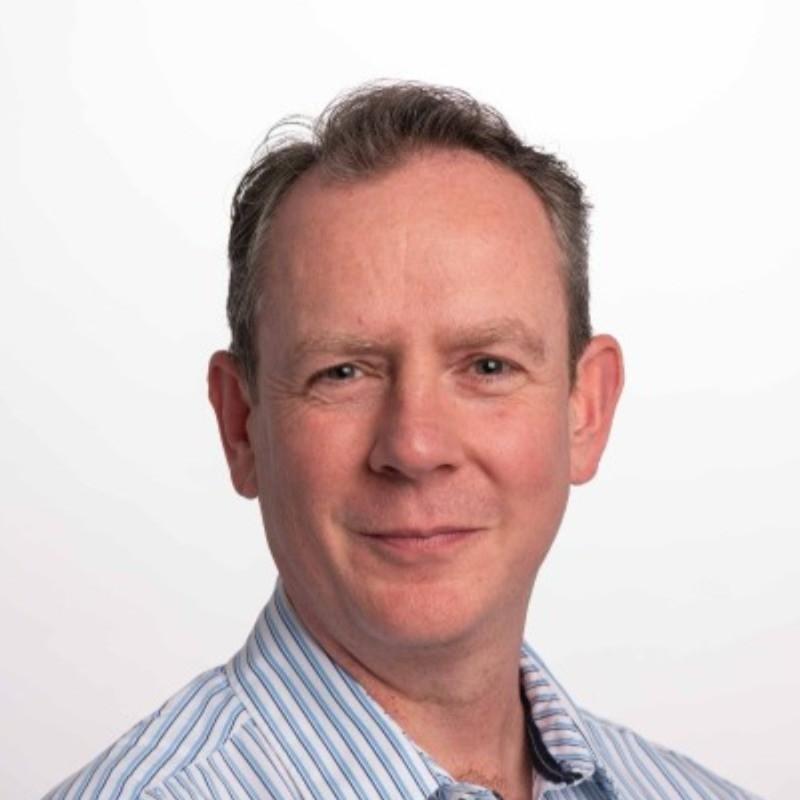 Head-and-shoulders portrait of a smiling man in a blue-striped shirt against a white background.