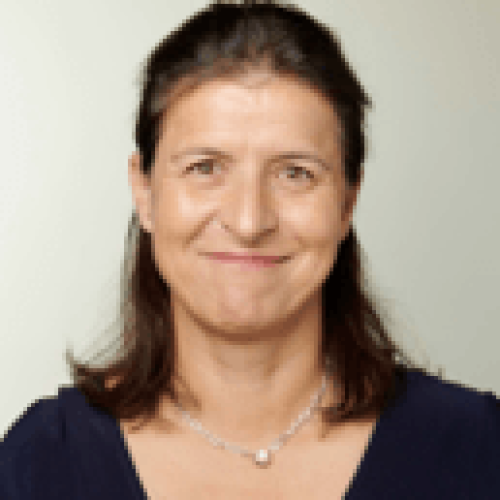 Portrait of a smiling woman with shoulder-length brown hair, wearing a navy blouse and a silver necklace against a light background.
