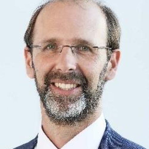 Portrait of a smiling man with glasses and a beard, wearing a blue blazer and white shirt.