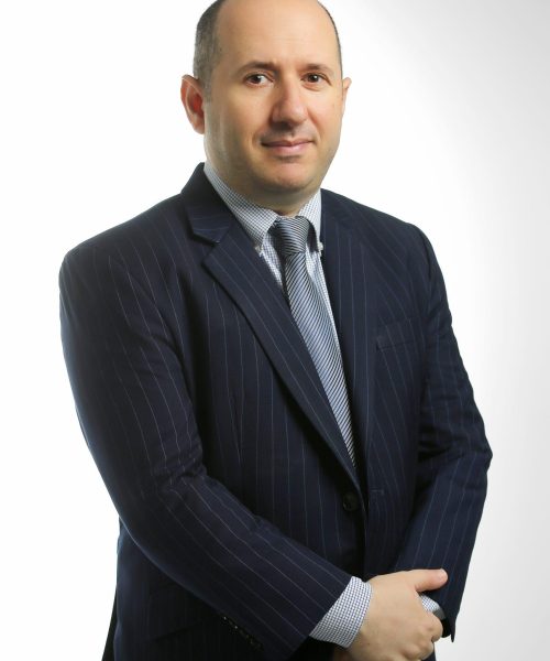 Professional portrait: man in a navy pinstripe suit with striped tie, arms crossed, looking at the camera.