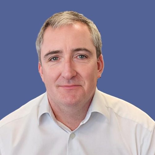 Head-and-shoulders portrait of a man with short gray hair in a white shirt against a blue background.