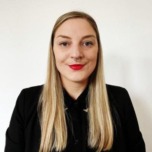 Professional headshot of a smiling blonde woman in a black blazer against a white background.